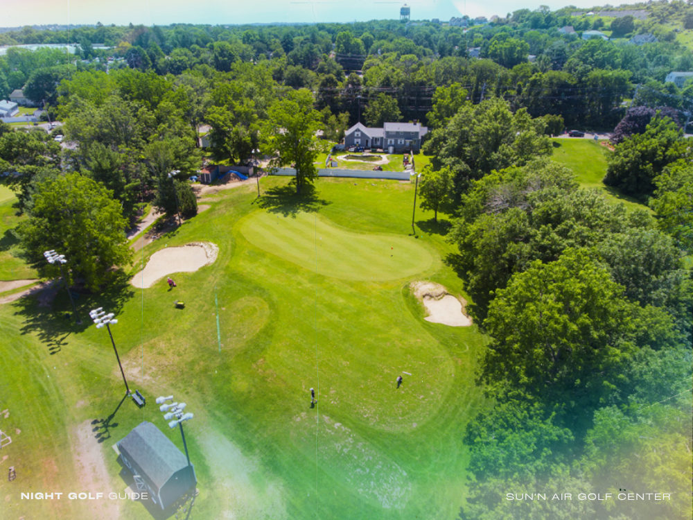 Sun'N Air Golf Center at night with bright course lighting, golfers practicing on the range, and clubhouse in view