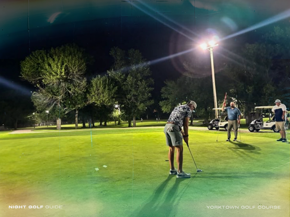 Golfers playing under floodlights at Yorktown's night golf course with scenic clubhouse nearby